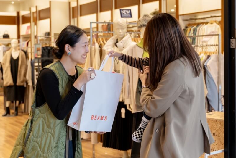 アパレルショップの出口で店員がお客様に商品を渡している様子